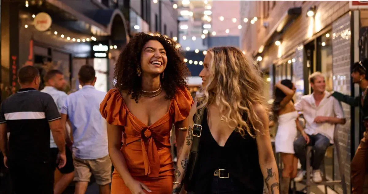 wo women walk down a lively street of bars at sunset in Adelaide