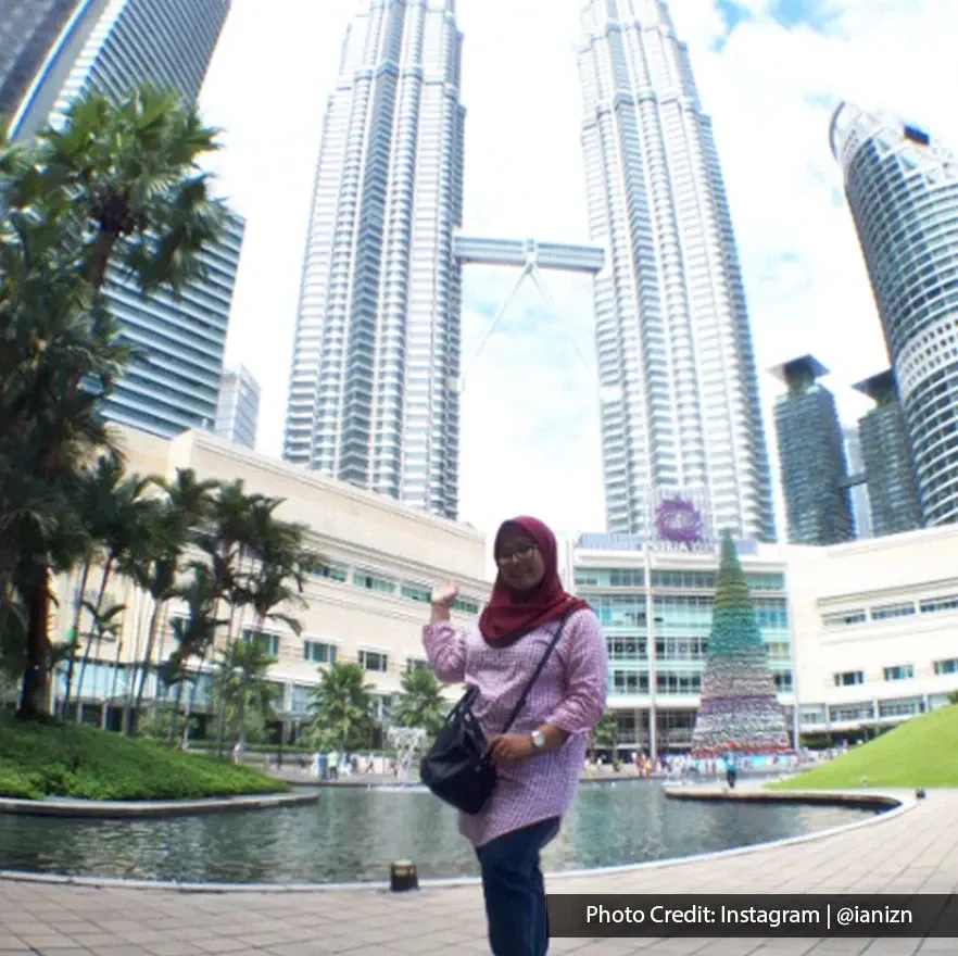Visitor posing in front of Suria KLCC lake with the Petronas Twin Towers behind