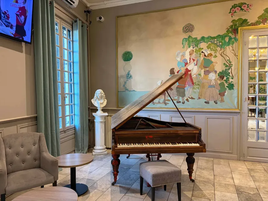 Salle élégante avec piano, fauteuils et une fresque colorée au mur du Grand Hôtel Molière.