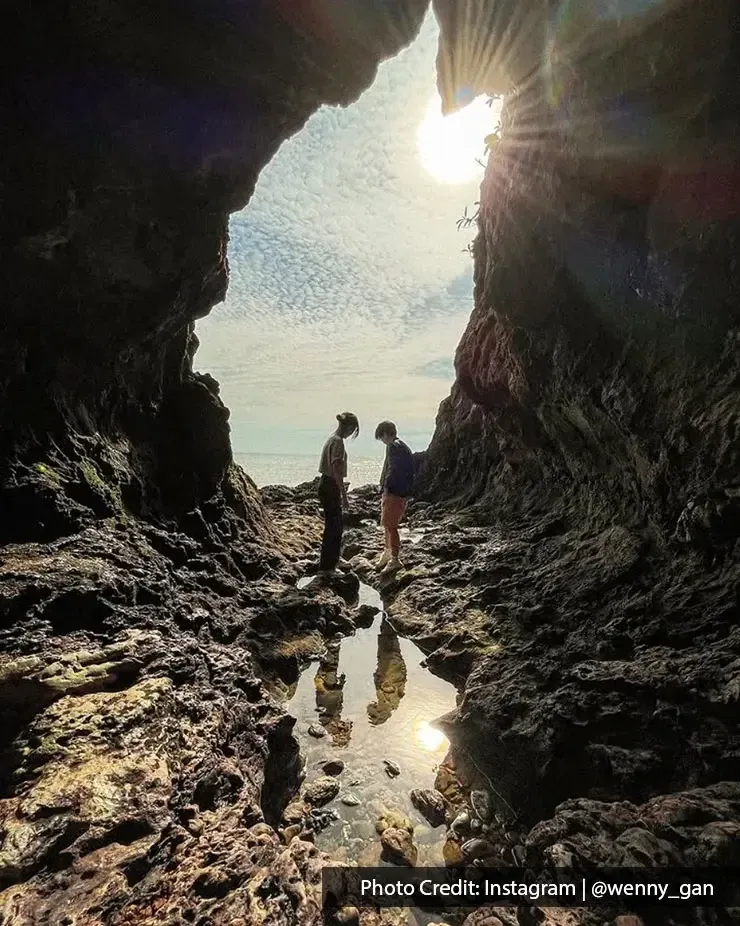 Dua individu berdiri di dalam gua berbatu dengan cahaya matahari atas gua - Lexis Hibiscus Port Dickson