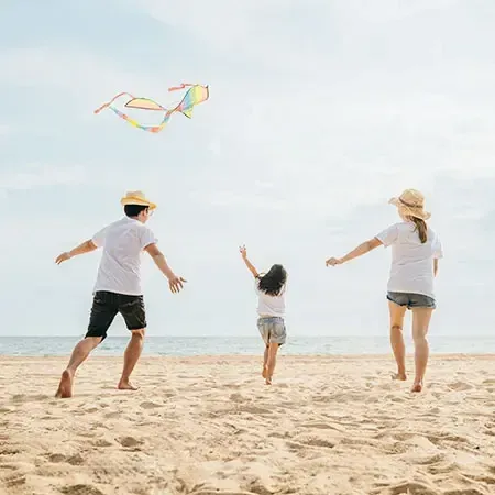 : A family flying a kite together at the beach during their beach vacation - Lexis MY