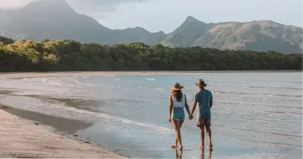 Two people walk along a beach with mountain views on Hinchinbrook Island, Townsville