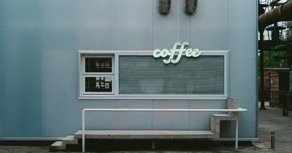 Minimalist Auckland coffee kiosk with metal siding and a neon “coffee” sign above a serving window.