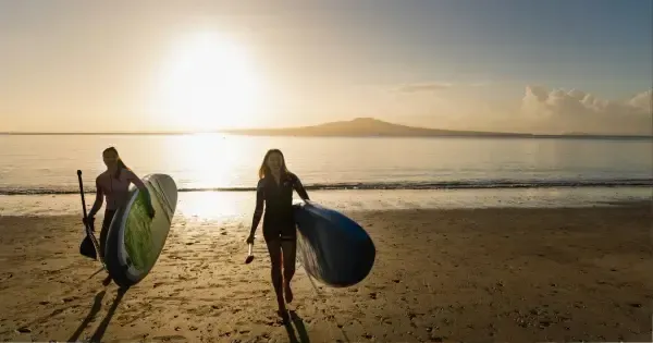 Two women with stand-up paddleboards at Takapuna, Auckland.