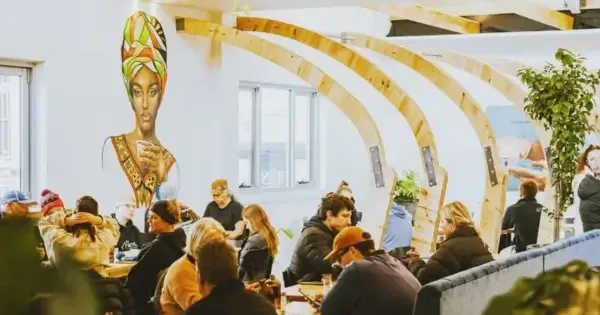 Café with diners, booth seating, plants, and a mural of a woman holding coffee