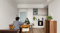 Two students talking at a dining table in a modern kitchen area with wooden furniture and appliances.