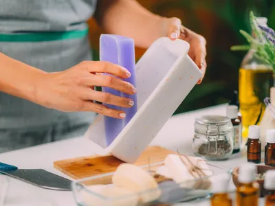 Woman crafting lavender-scented soap in a mold surrounded by botanicals and oils.