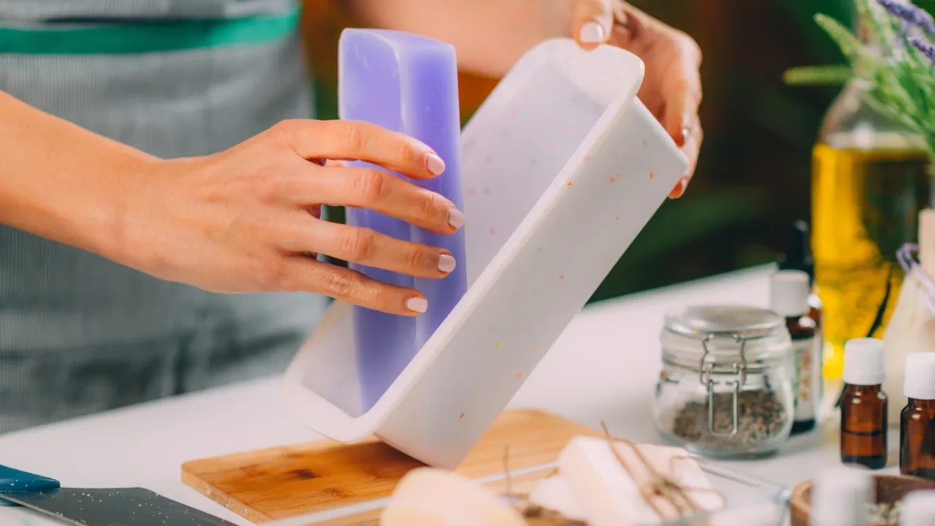 Woman crafting lavender-scented soap in a mold surrounded by botanicals and oils.