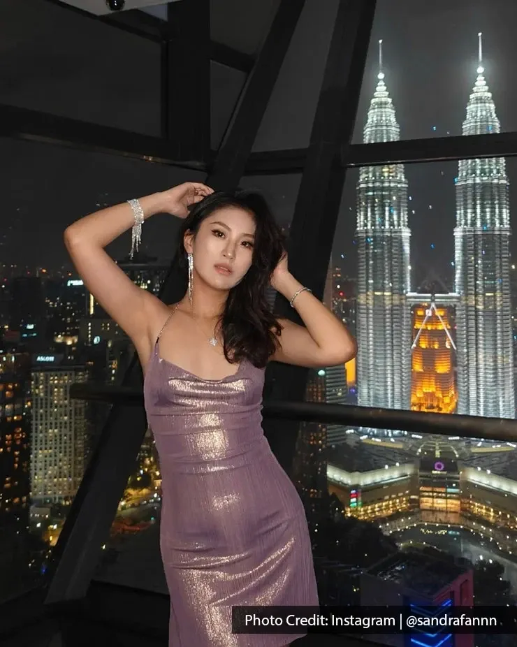 A woman poses in a shiny dress with Petronas Twin Towers in the background at night.