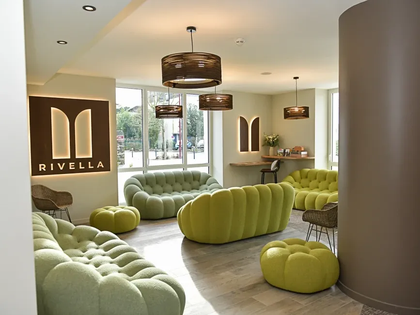 Salon confortable avec mobilier vert et luminaires suspendus chez Hôtel Rivella.