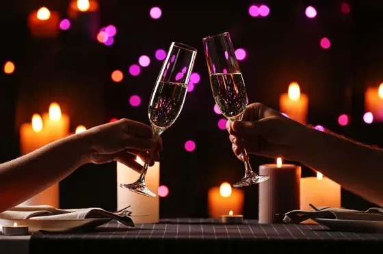 A close-up of two hands clinking wine glasses, surrounded by candlelight.