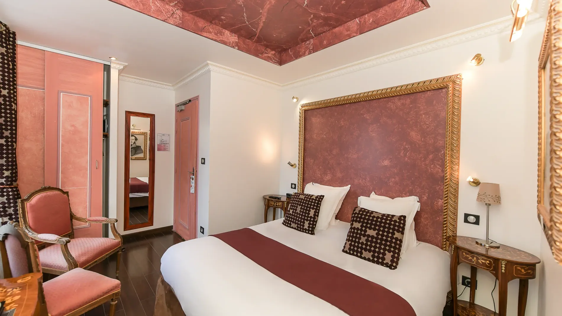 Elegant hotel room with ornate bed, pink walls, and wooden floors at The Originals Boutique, Hôtel Villa Aultia.