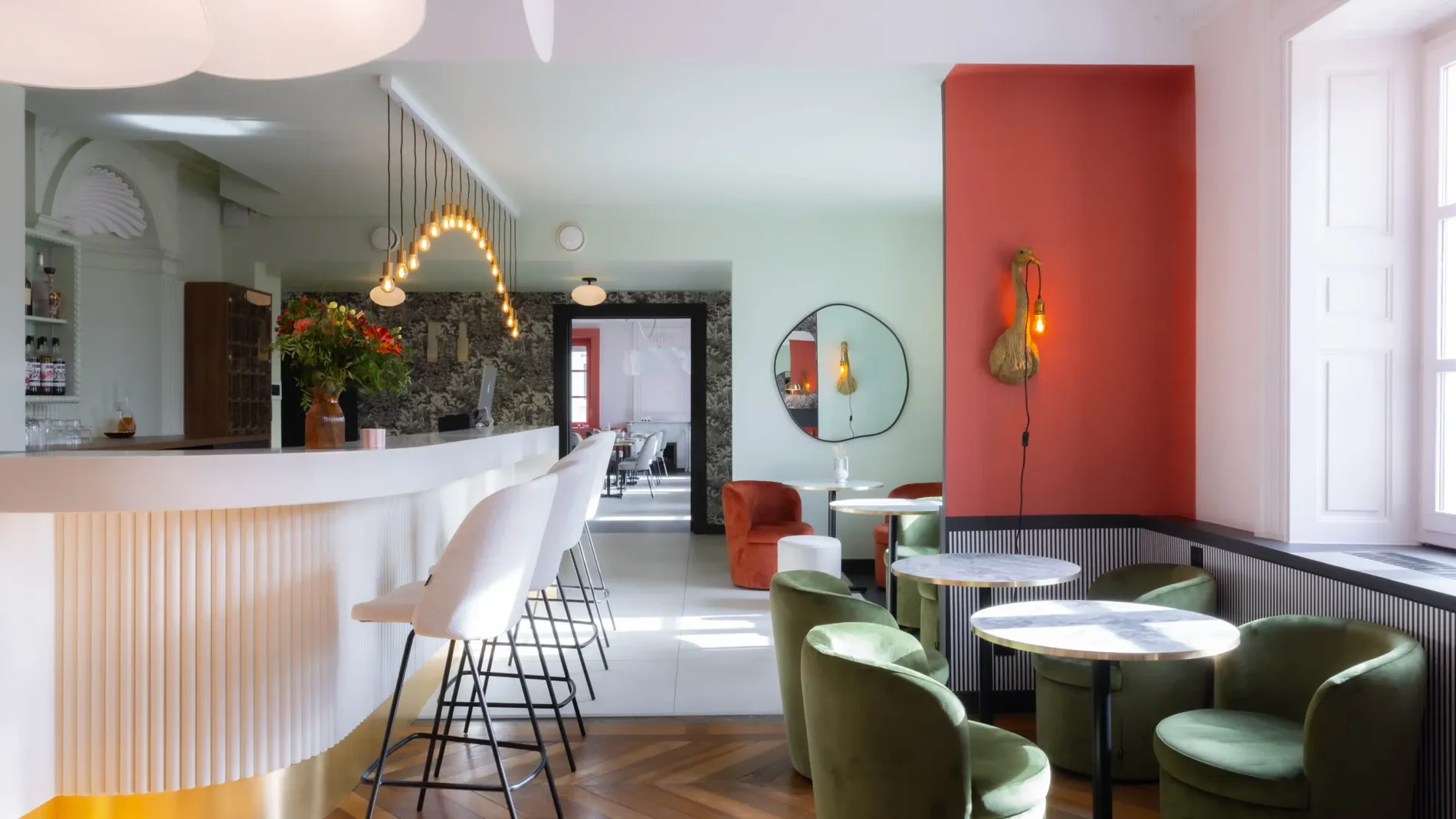 Lounge bar with white curved service counter and green velvet armchairs around round cafe tables at Hôtel 2M