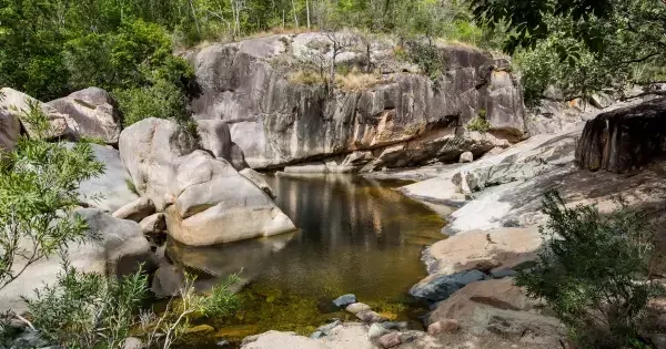 Rock pool surrounded by large boulders and lush green bushland
