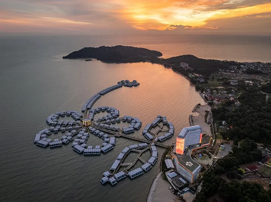 Aerial view of overwater villas along a tropical coastline during sunset.