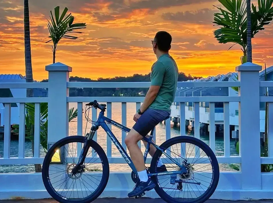 A man sitting on a bicycle, watching the sunset at a beach resort in Malaysia- Lexis MY