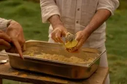 Hands grating fresh ingredients over a stainless steel food pan during an open-air cooking class outside at Unika Hotels