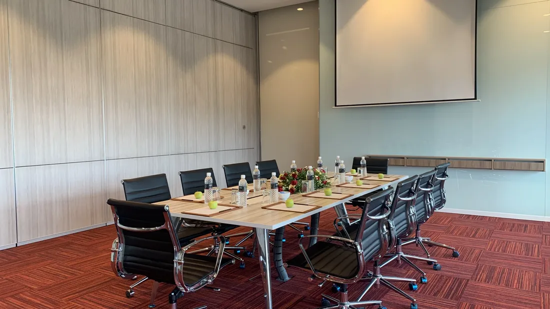 Meeting room with long table, chairs, and projector screen for events.