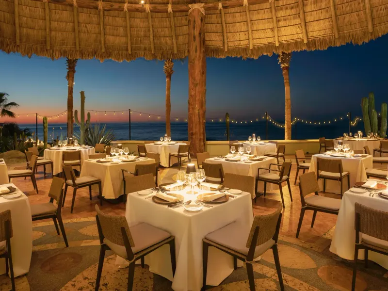 Outdoor dining area at the Hacienda del Mar Los Cabos All Includes Resort overlooking the ocean at dusk.