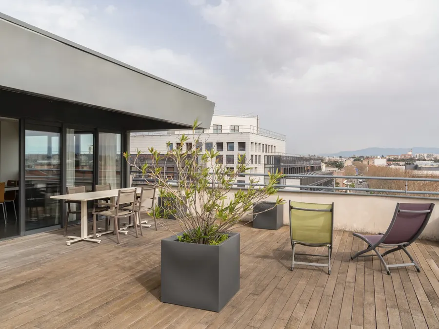 Modern two-bedroom apartment terrace with furniture and cityscape view at Appart’Hôtel Hévéa in Valence.