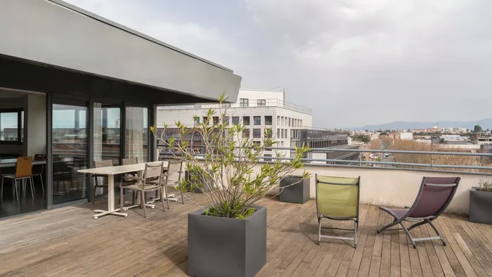 Outdoor terrace with dining area and lounge chairs at Appart’Hôtel Hévéa.