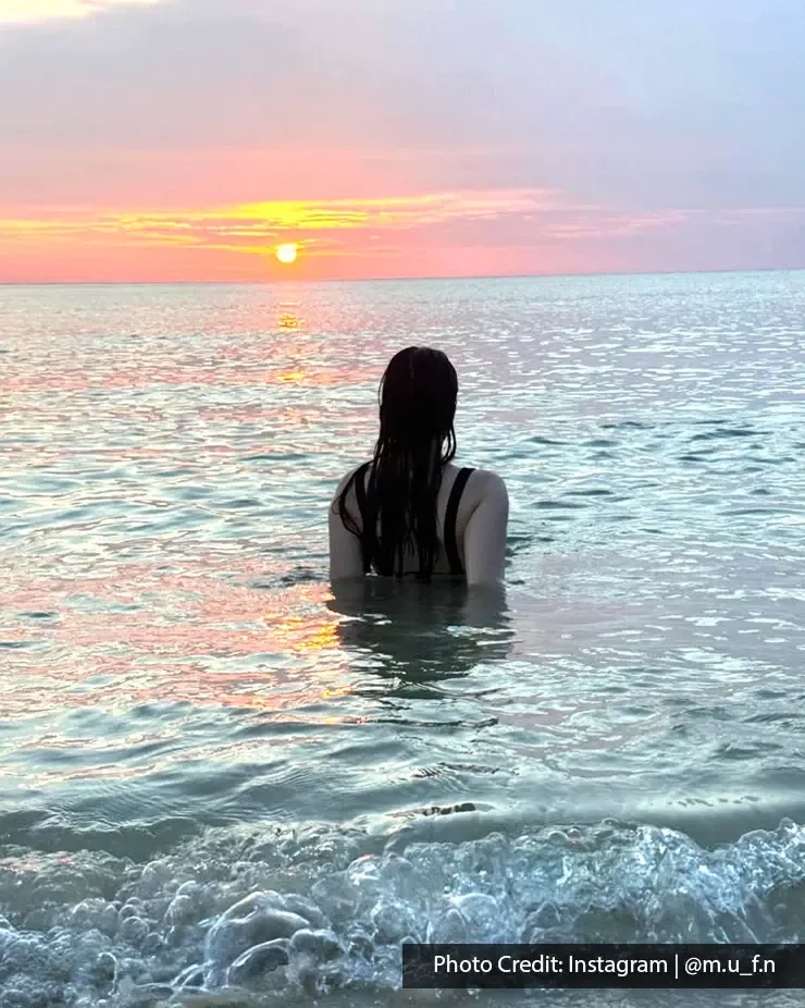 Person standing in sea facing sunset.