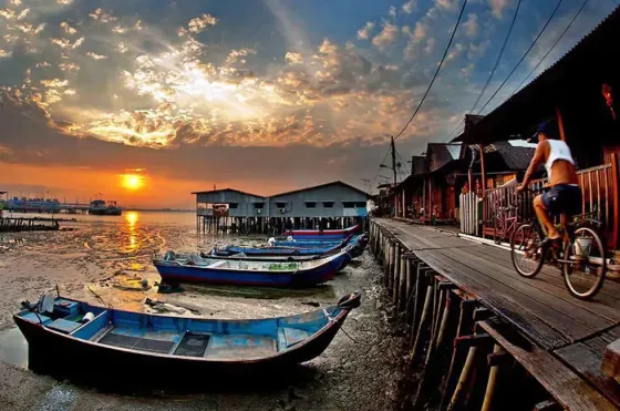 A man pedals his bike along the dock, bathed in the warm glow of sunset - Lexis Suites Penang