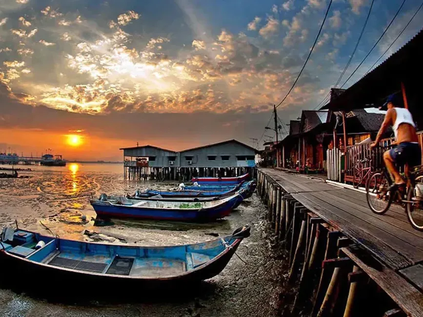 A man pedals his bike along the dock, bathed in the warm glow of sunset - Lexis Suites Penang