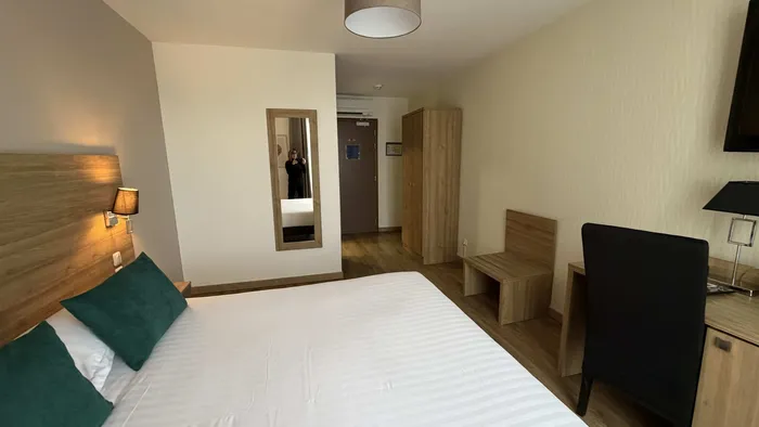 Chambre avec lit blanc, oreillers verts et mobilier en bois au Grand Hôtel Molière.