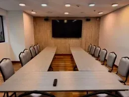 Meeting room with U-shaped tables and gray chairs facing a wall-mounted TV at Unika Hotels, the Colombia event center
