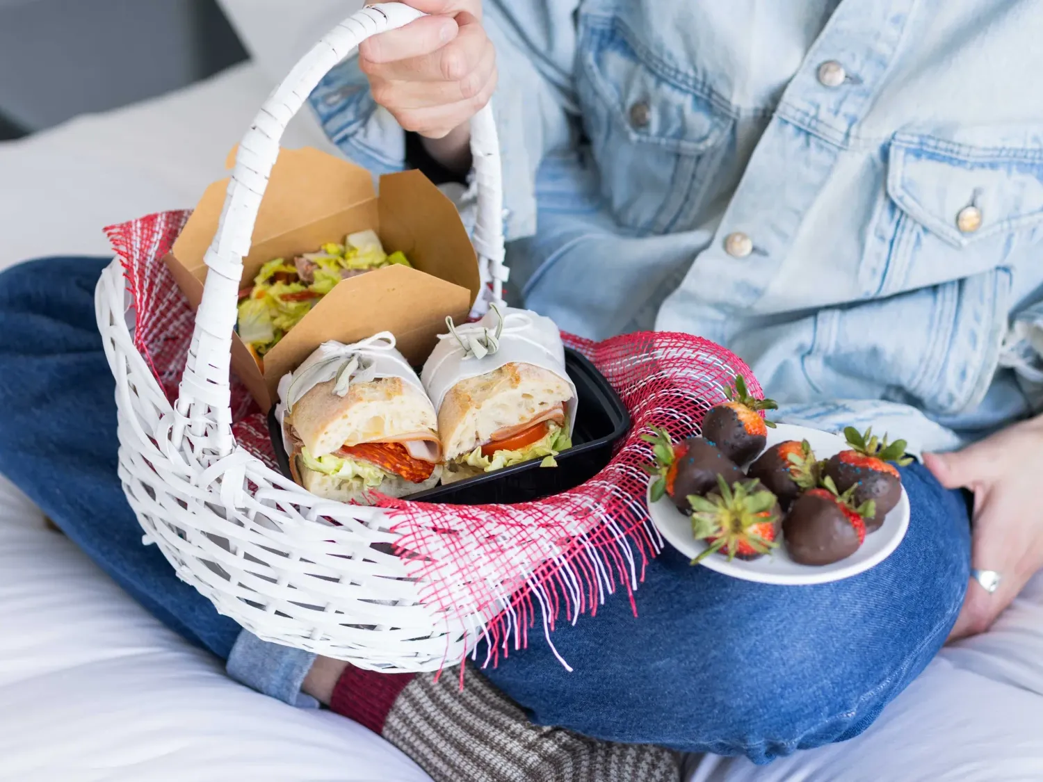 White picnic basket filled with a sandwich and salad, with a plate of chocolate at The Godfrey Hotel Hollywood