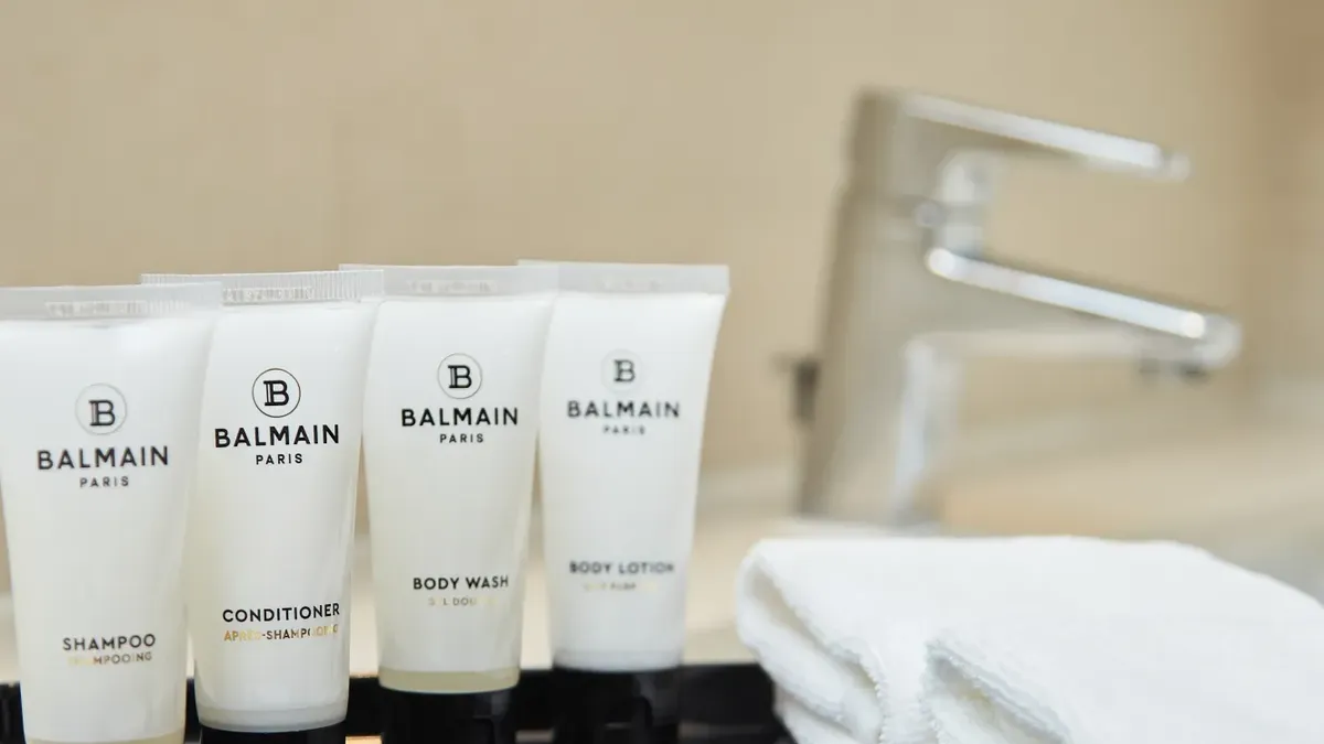 Four Balmain Paris tubes, towels, and a soap bar on a black tray on a bathroom sink.