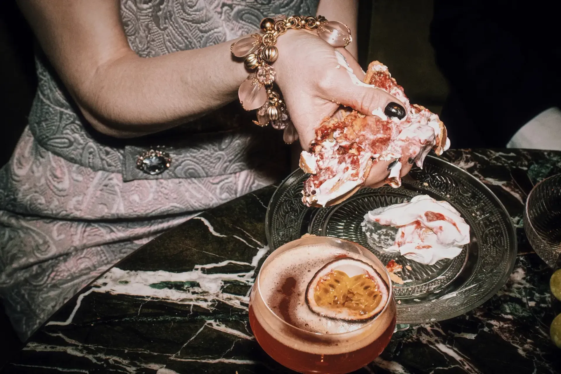 Hand with rose gold bracelet reaching for layered dessert beside cocktail with citrus garnish at Hotel Motto