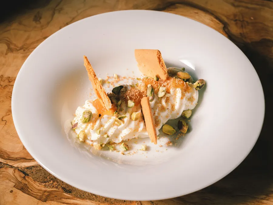 Dessert avec crème, pistaches et caramel sur assiette blanche de Masseria Stali.