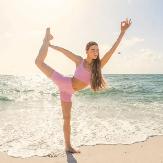 Woman performing a yoga pose on the beach with ocean waves in the background.