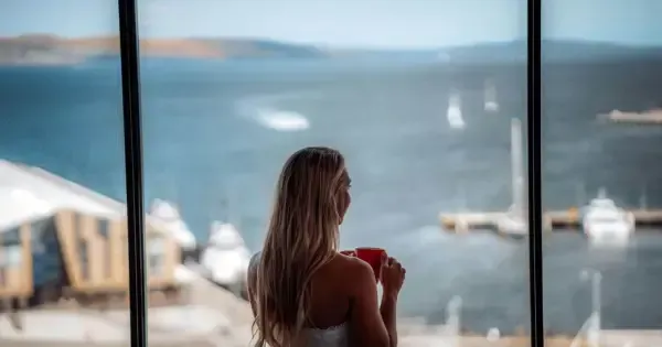 Woman stands in the window of her suite with a coffee at the Hotel Grand Chancellor Hobart
