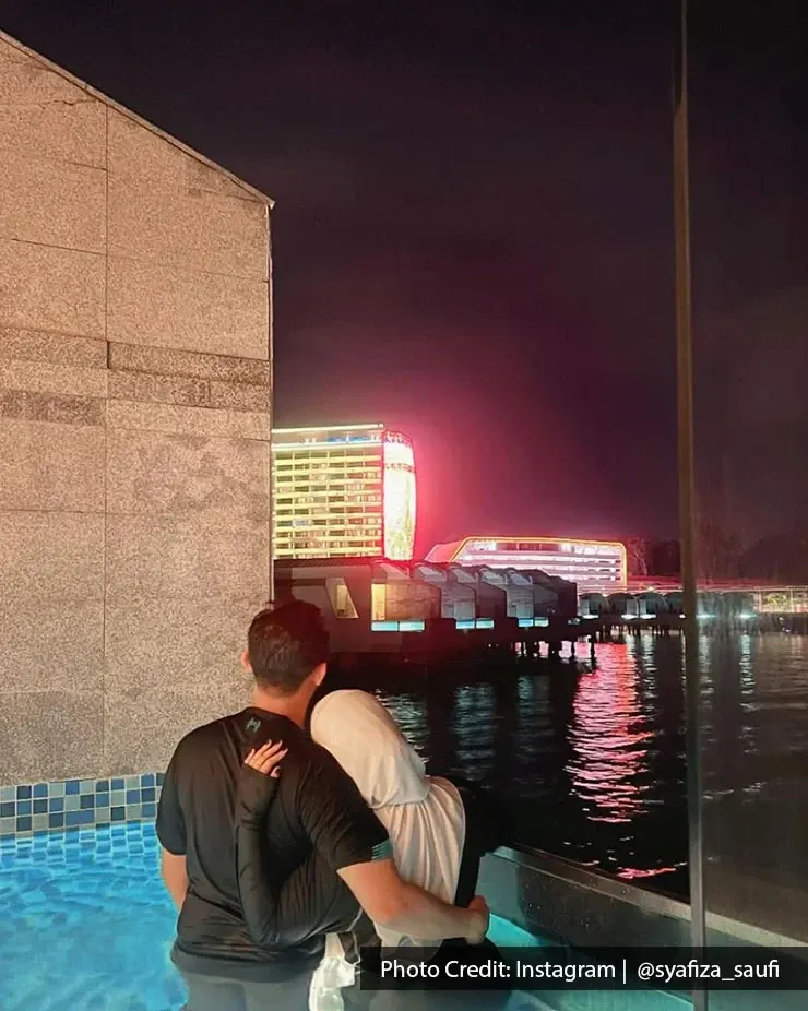 Couple relaxing in a pool at night with colorful resort lights.