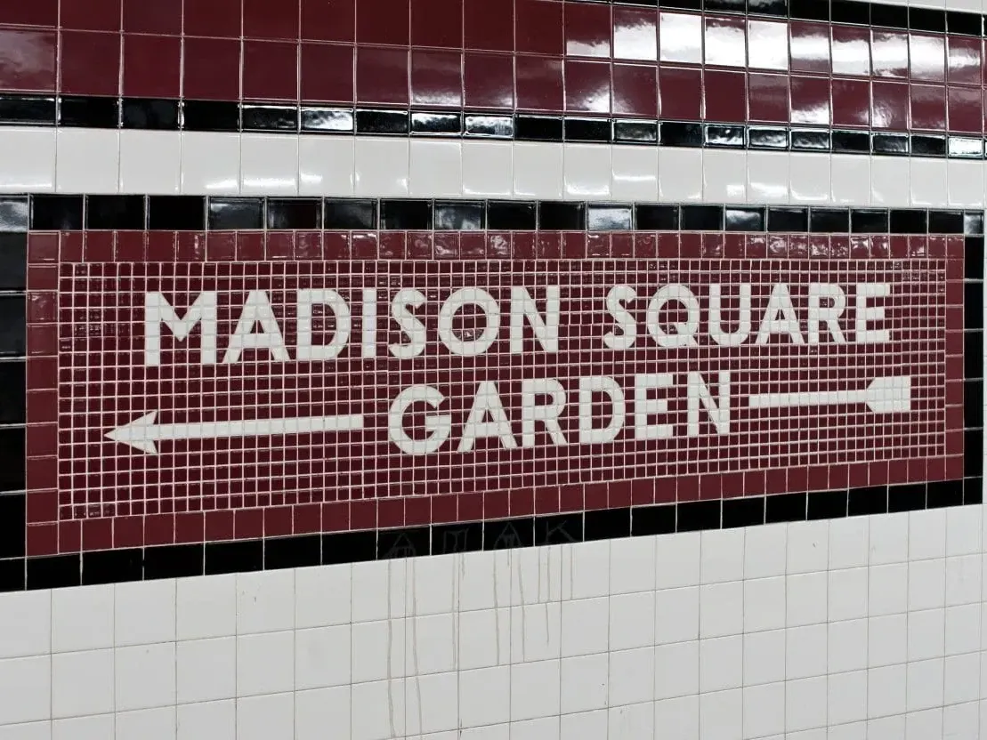 Signage for Madison Square Garden displayed on subway tiles, with directional arrows near Kixby Hotel