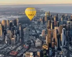 Yellow hot air balloon flying over the tall Melbourne city skyline near Amora Hotel Riverwalk Melbourne at sunrise