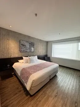 Spacious king bed under mural art beside large bright windows on hardwood floors inside guestroom at Hotel B3 Virrey