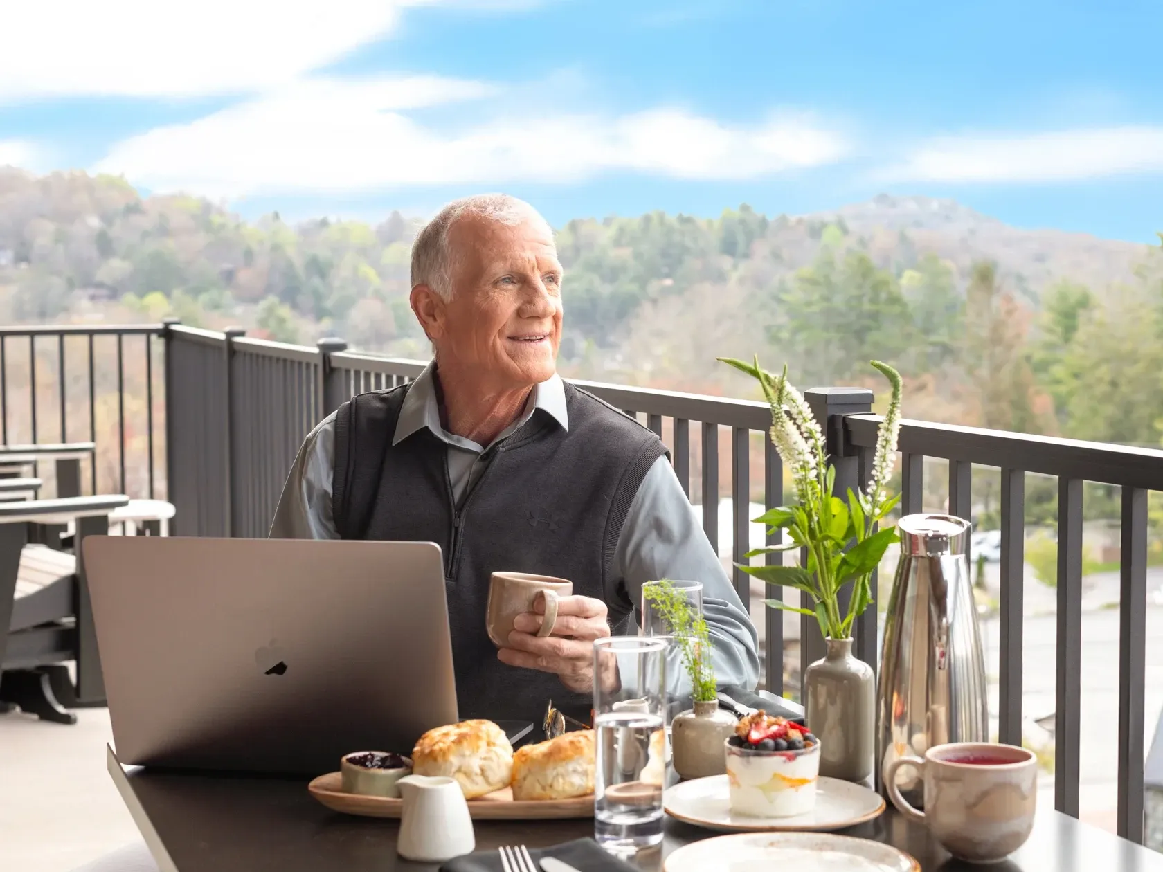 Business traveler working on laptop while enjoying breakfast on outdoor terrace with scenic mountain views.