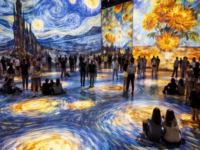 Large crowd gathered around immersive art exhibit with swirling Van Gogh paintings on walls.