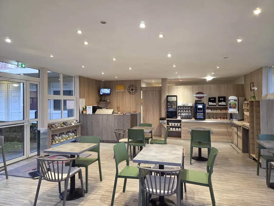 Salon de café avec tables et chaises vertes à l'Hôtel Aurillac Aéroport.