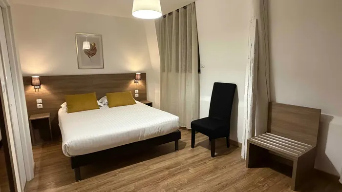 Chambre moderne avec lit double, chaise et luminaires chaleureux chez Le Grand Hôtel Molière.