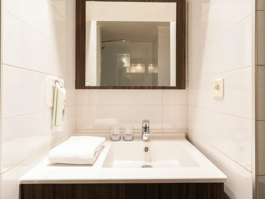 Bathroom with a white sink, mirror, and shower, part of the Standard Studio at Appart’Hôtel Hévéa, Valence.