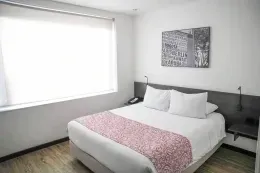 Guest room with a white bed and pink runner by a bright window at Unika Hotels, one of the best locations to stay in Bogota