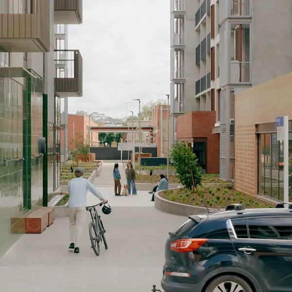 Pedestrian walking with a bicycle on a pathway surrounded by modern buildings and greenery.