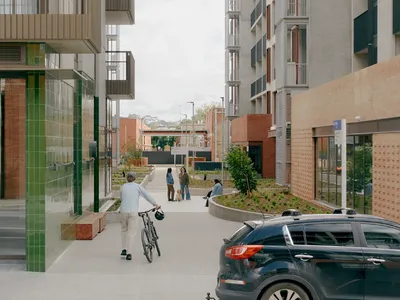 Pedestrian walking with a bicycle on a pathway surrounded by modern buildings and greenery.