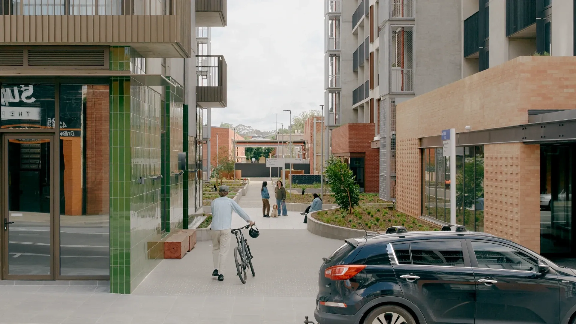 Pedestrian walking with a bicycle on a pathway surrounded by modern buildings and greenery.