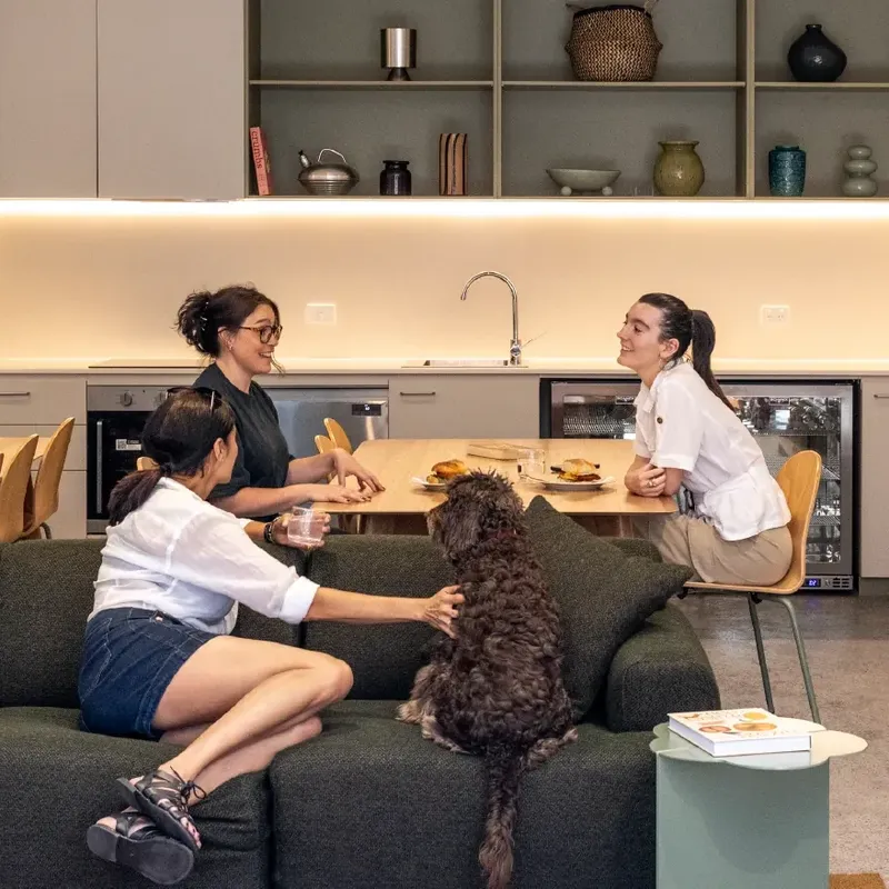 Three women and a dog enjoying a meal in a modern apartment kitchen.